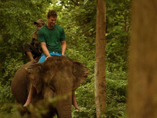 A tourist riding on the elephant with a trainer