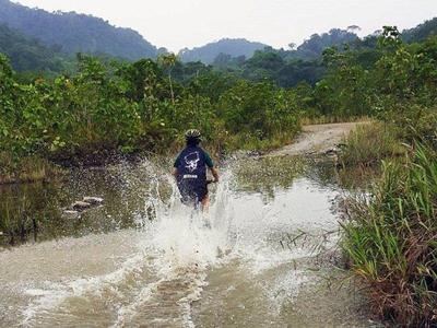 Cycling tourist pedalling through a river in Kuching