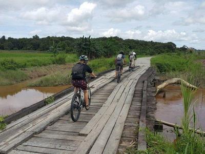 Tourists cycle across a wooden bridge in countryside of Kuching